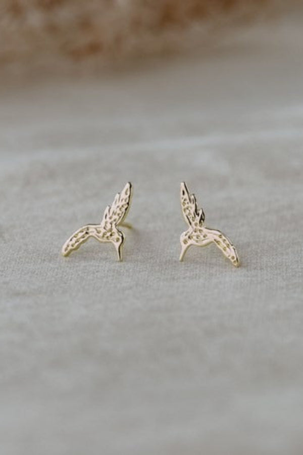 Gold bird-shaped earrings on a light gray surface