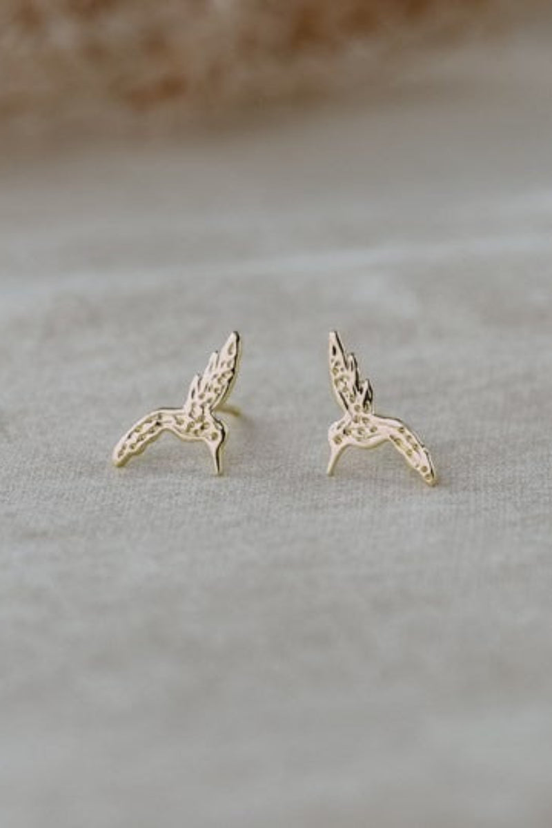 Gold bird-shaped earrings on a light gray surface