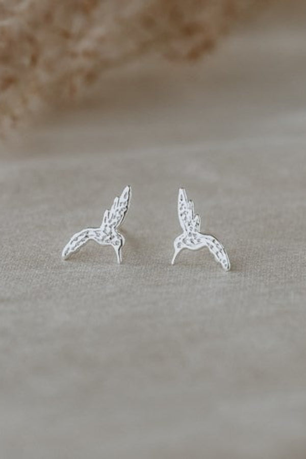 Silver bird-shaped earrings on a beige fabric background