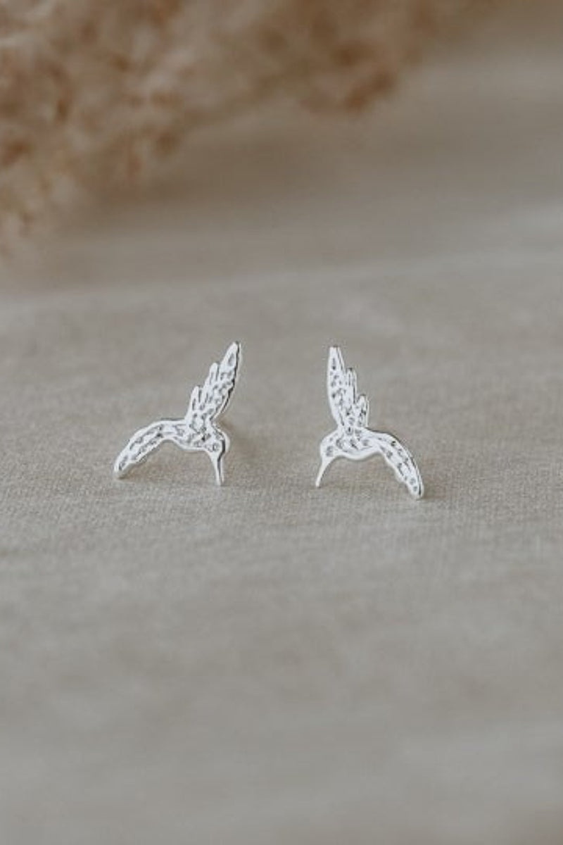 Silver bird-shaped earrings on a beige fabric background