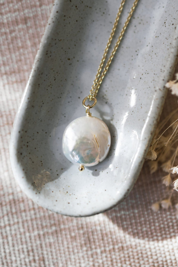 Necklace with a round pendant on a textured surface with dried flowers
