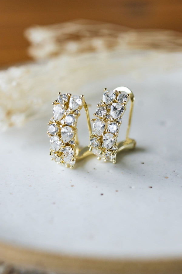 Gold earrings with clear stones on a textured white surface