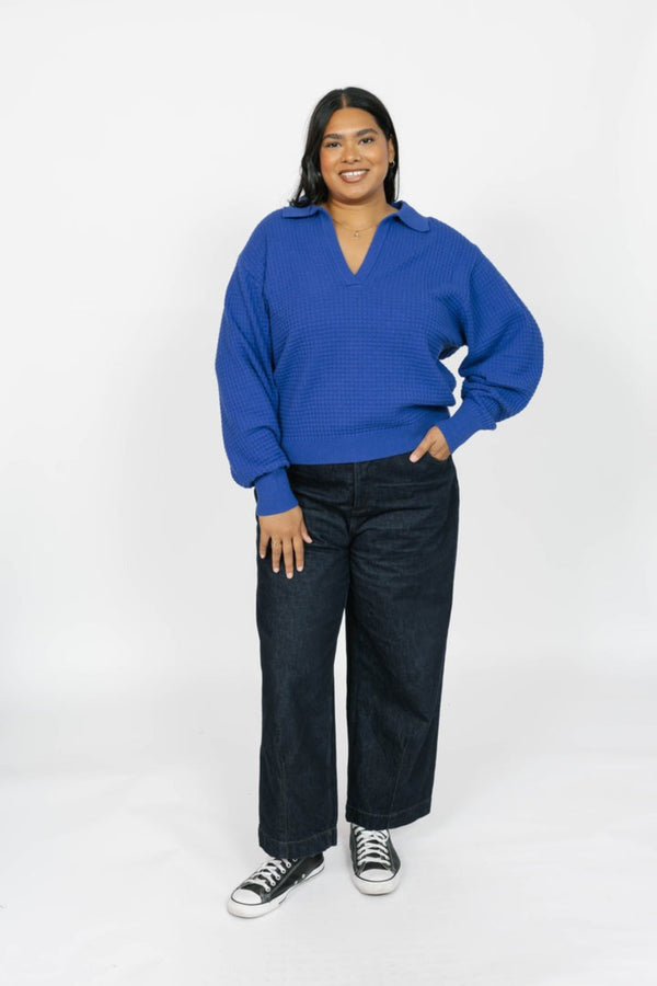Person wearing a blue sweater and dark jeans on a white background