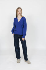 Woman wearing a blue sweater and dark jeans on a white background