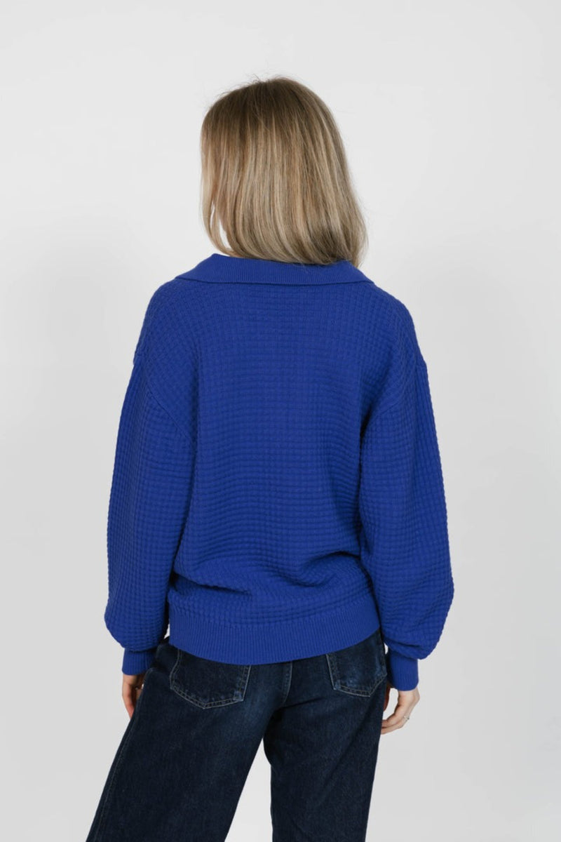 Person wearing a blue sweater and dark jeans on a white background