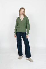 Woman wearing a green sweater and dark blue jeans on a white background