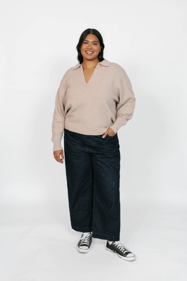 Person wearing a beige sweater and black pants on a white background