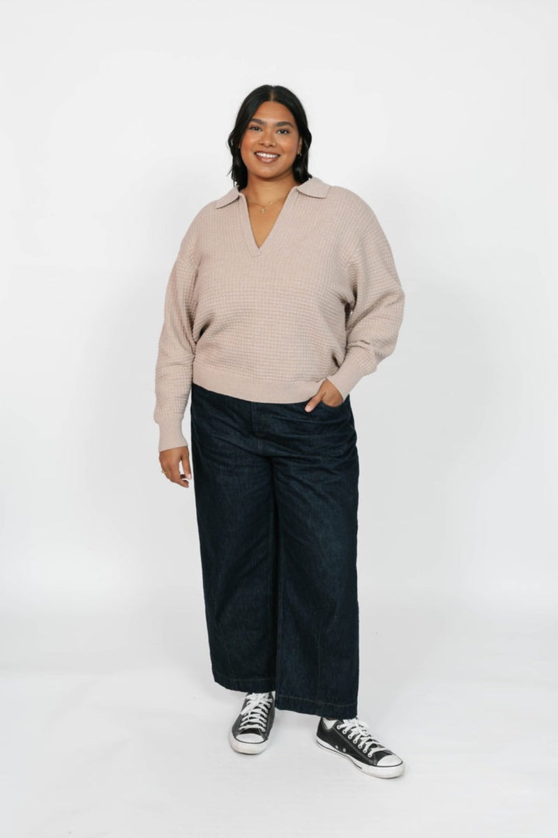 Person wearing a beige sweater and black pants on a white background