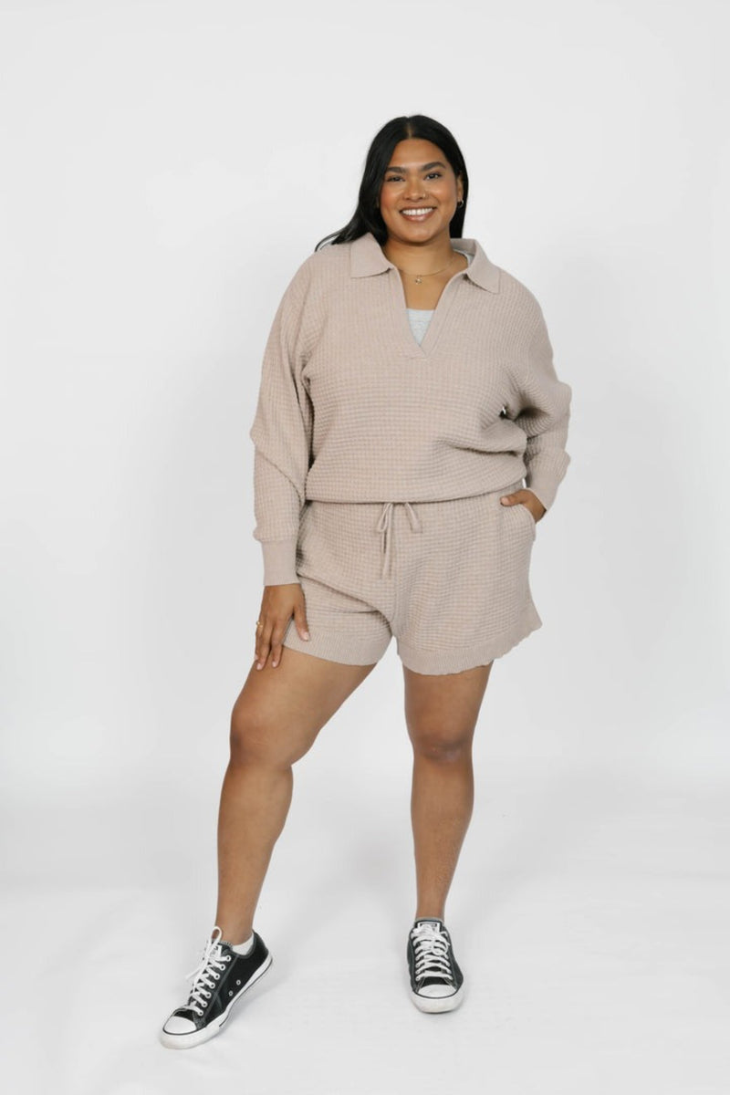 Person wearing a beige outfit with shorts and a long-sleeve top on a white background