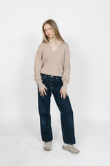 Woman wearing a beige sweater and dark jeans on a white background