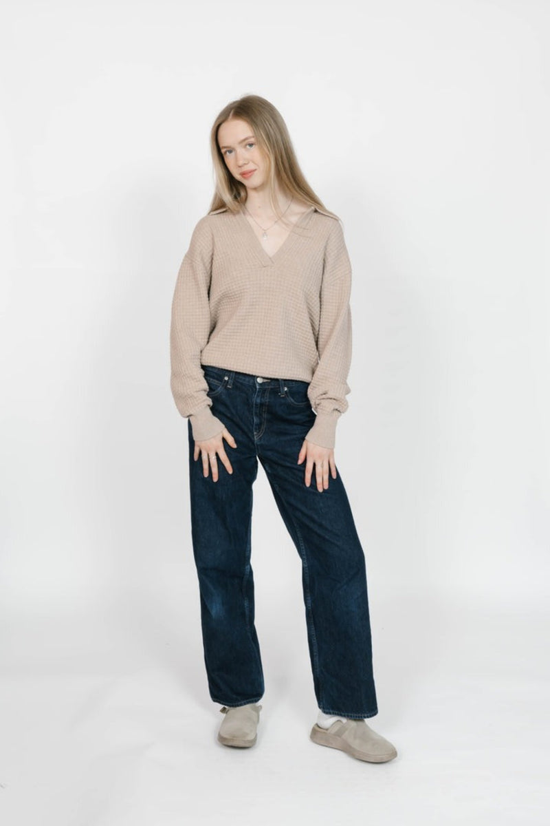 Woman wearing a beige sweater and dark jeans on a white background