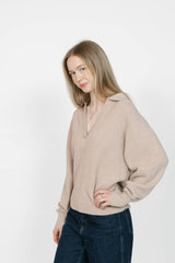 Woman wearing a beige sweater and dark jeans against a white background