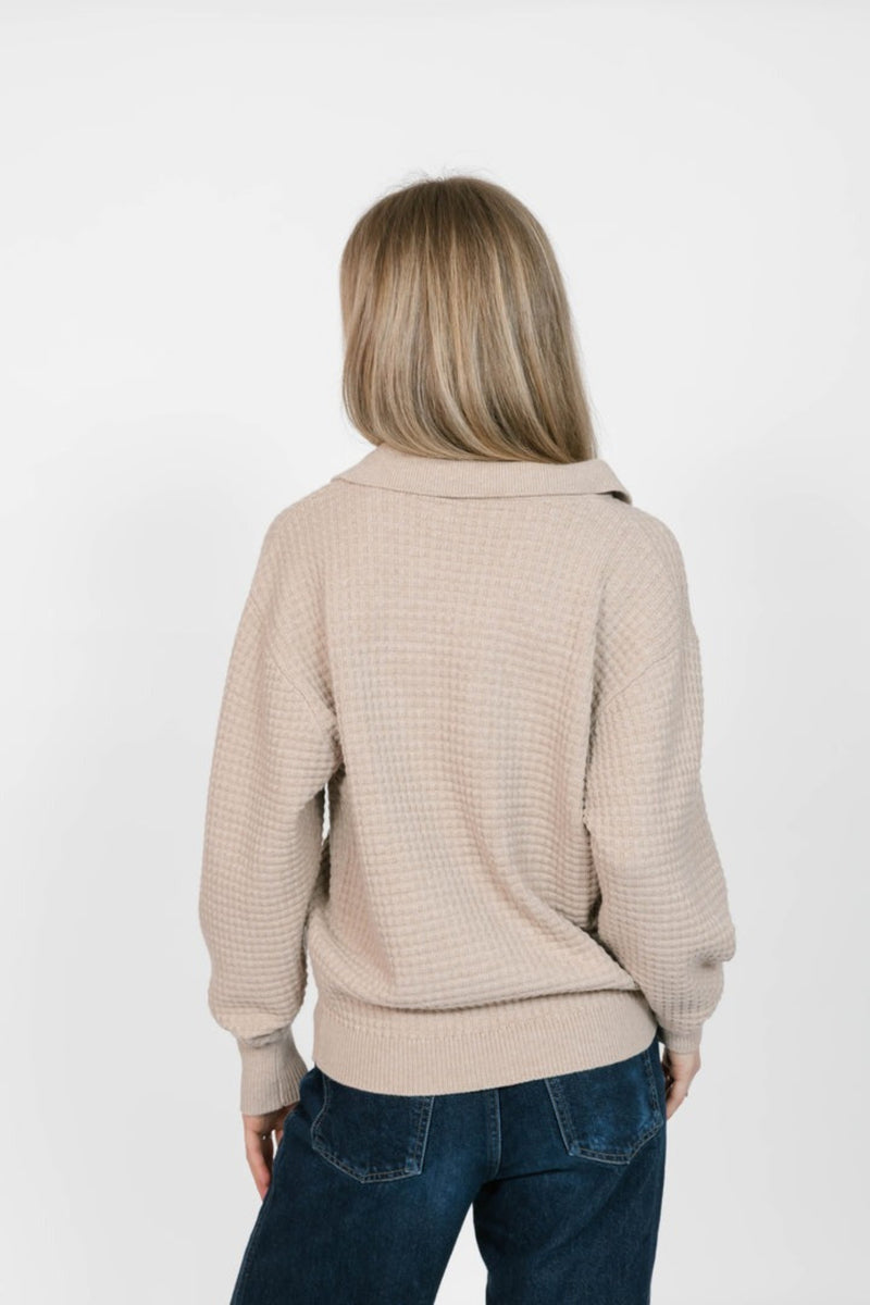 Person wearing a beige sweater and blue jeans on a white background