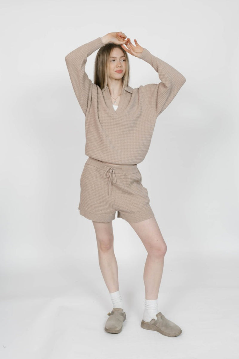 Person wearing a beige sweater and shorts set on a white background