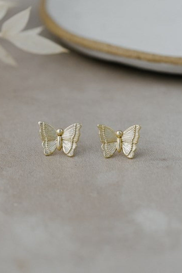 Gold butterfly earrings on a neutral background