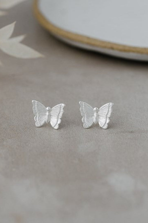 Silver butterfly earrings on a neutral surface with a blurred background