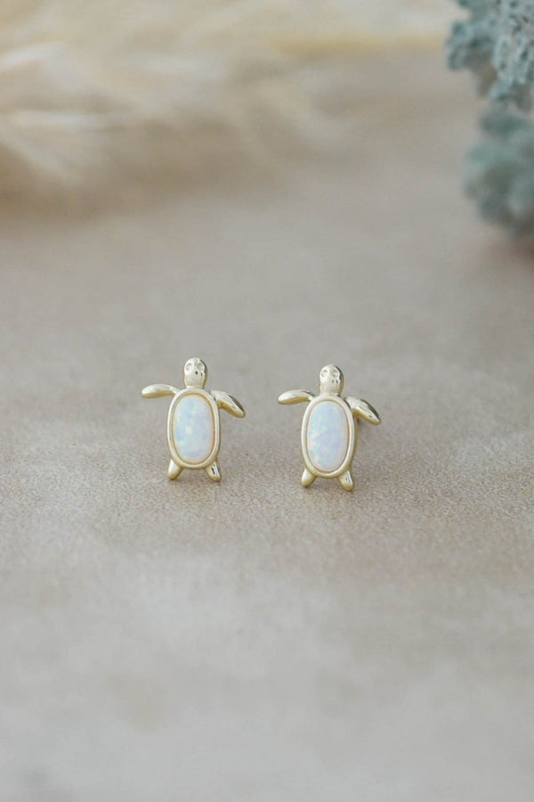 Turtle-shaped earrings with opal stones on a soft beige background