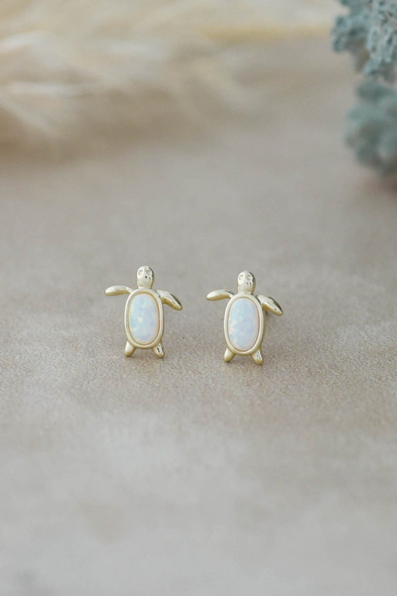 Turtle-shaped earrings with opal stones on a soft beige background