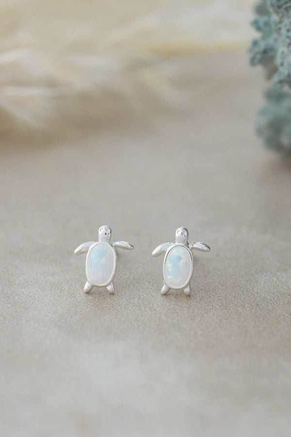 Turtle-shaped earrings with opal-like stones on a neutral background