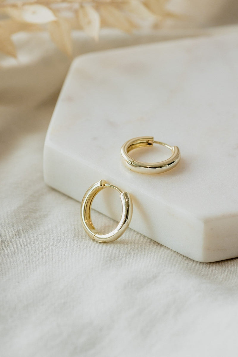 A pair of small gold circular hoop earrings displayed on a white marble surface.