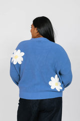 Person wearing a blue sweater with white daisy patterns on a plain background