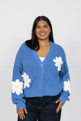 Woman wearing a blue cardigan with white floral patterns on a plain background