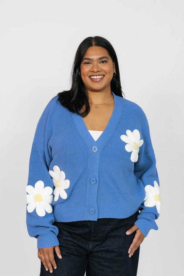 Woman wearing a blue cardigan with white floral patterns on a plain background