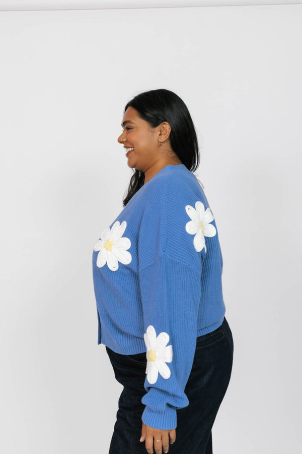 Person wearing a blue sweater with white daisy patterns on a plain background