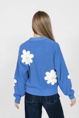 Person wearing a blue sweater with white daisy patterns on a plain background