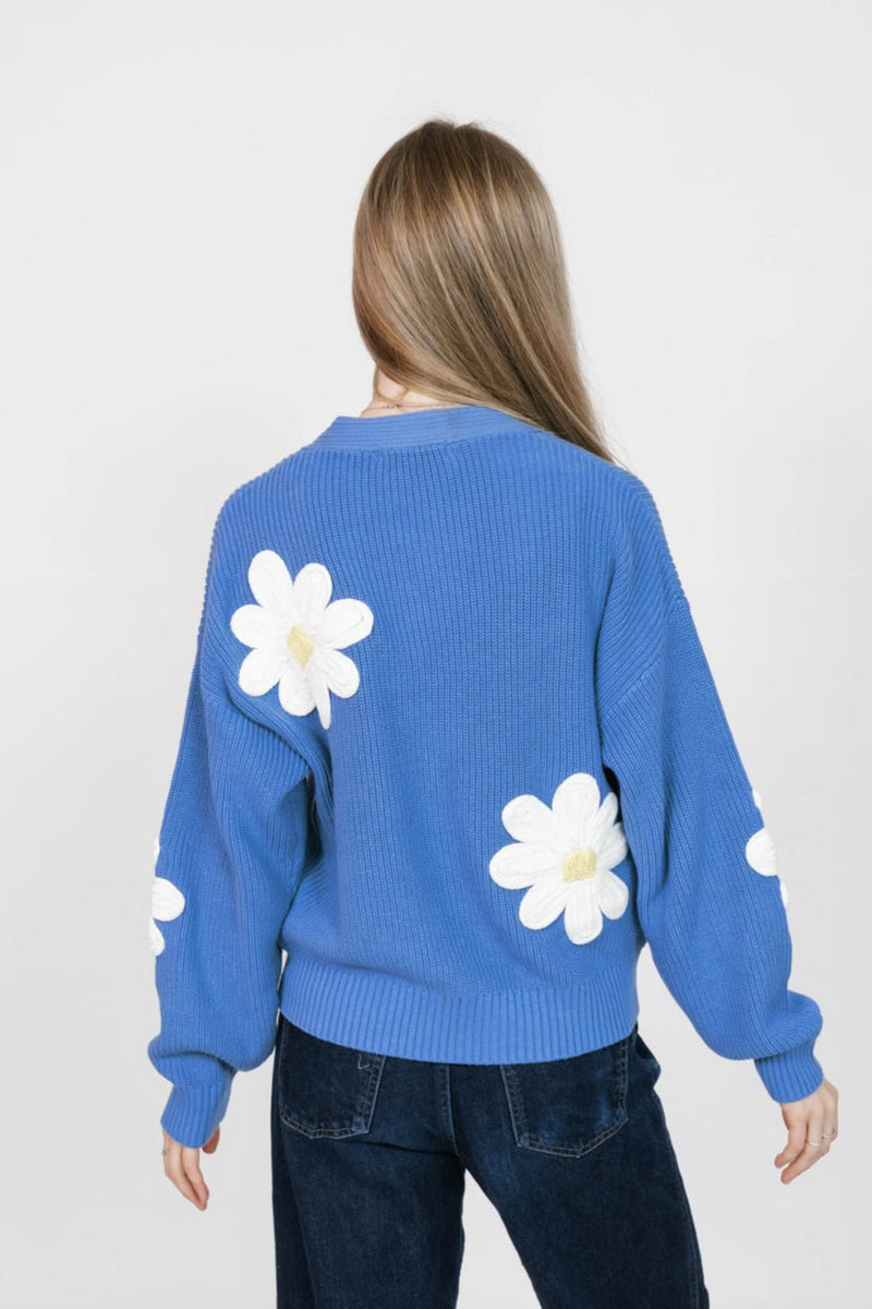 Person wearing a blue sweater with white daisy patterns on a plain background