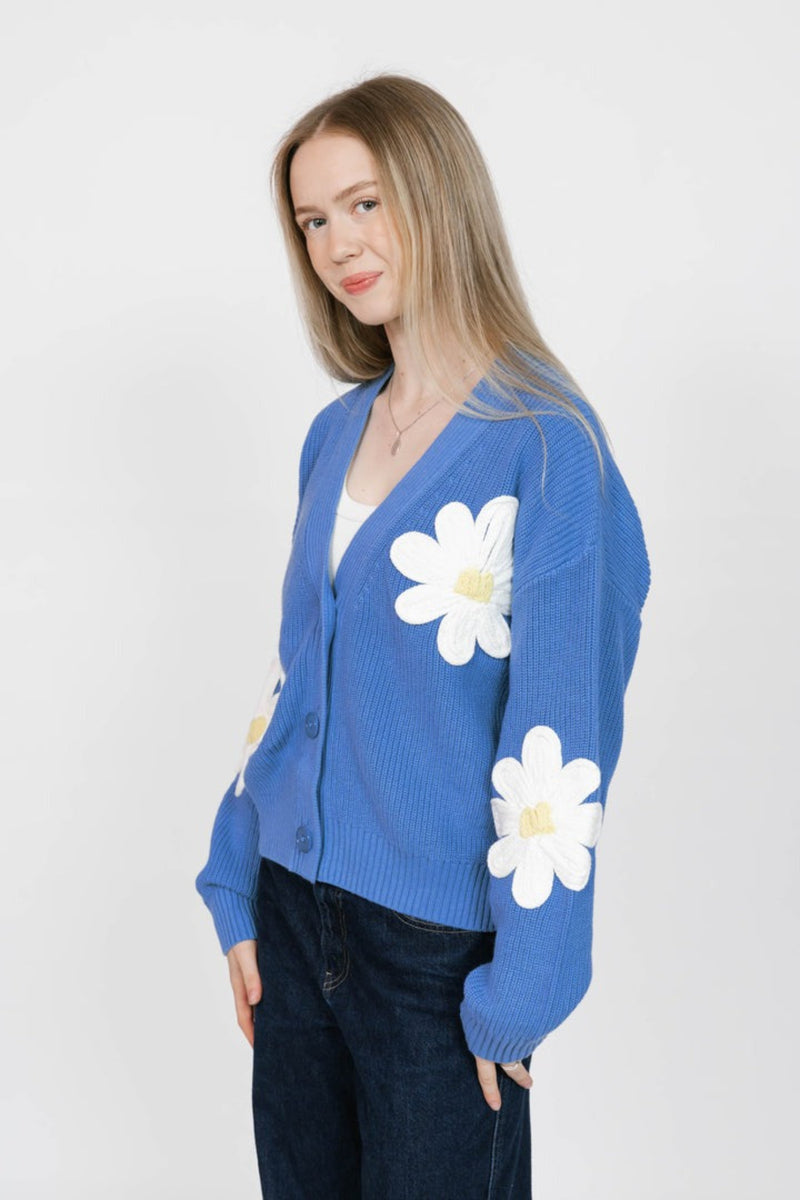 Woman wearing a blue cardigan with white daisy patterns on a white background