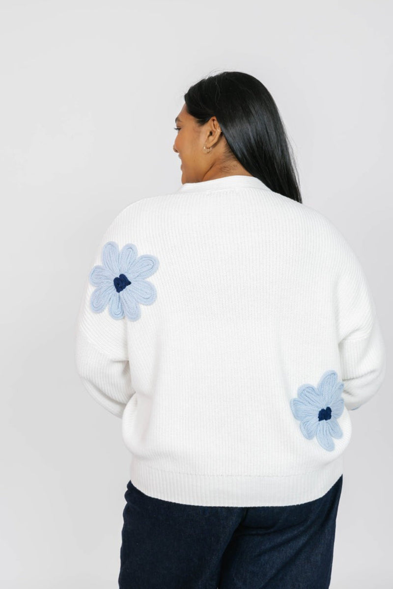 Person wearing a white sweater with blue floral patterns on a plain background