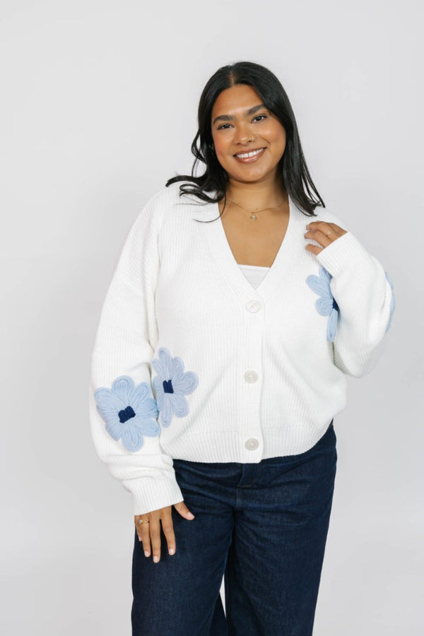 Woman wearing a white cardigan with blue flower patterns on a plain background
