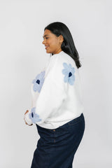 Woman wearing a white sweater with blue floral patterns on a plain background