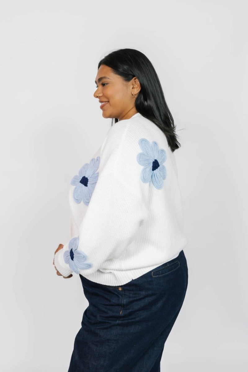 Woman wearing a white sweater with blue floral patterns on a plain background