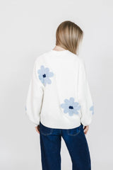 Person wearing a white sweater with blue floral patterns on a plain background