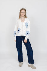 Woman wearing a white cardigan with blue floral patterns and blue jeans on a white background