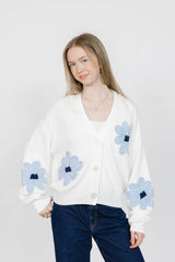 Woman wearing a white cardigan with blue floral patterns on a plain background