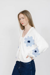 Woman wearing a white sweater with blue floral patterns on a white background