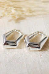 Pair of silver geometric earrings on a textured beige fabric background