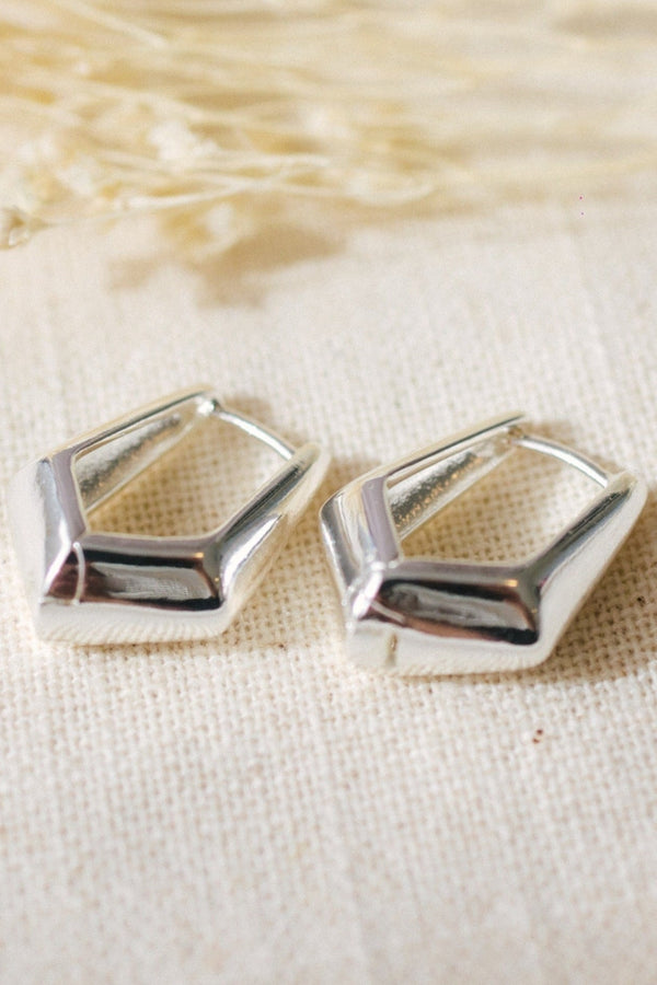 Pair of silver geometric earrings on a textured beige fabric background