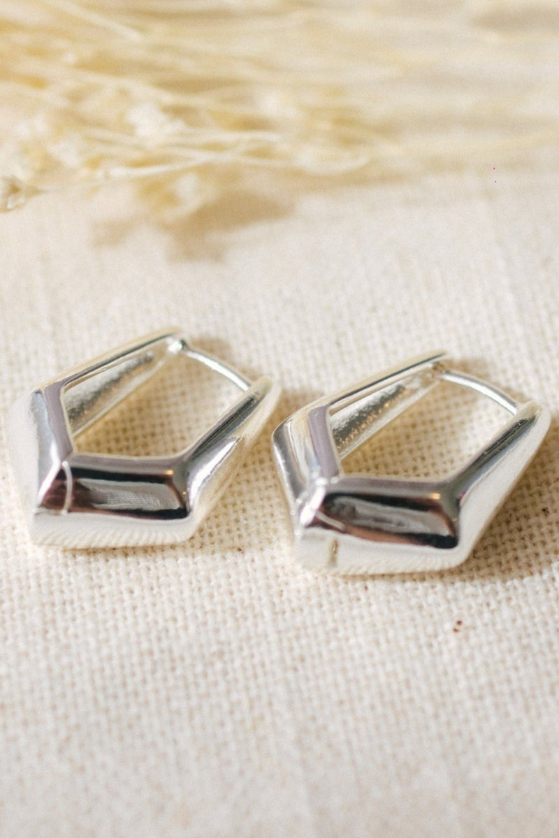 Pair of silver geometric earrings on a textured beige fabric background
