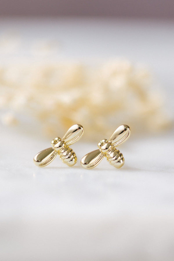 Gold bee-shaped earrings on a soft white background