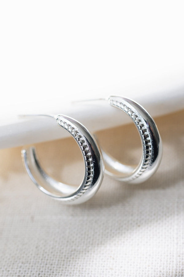 Silver hoop earrings on a white surface with a blurred background