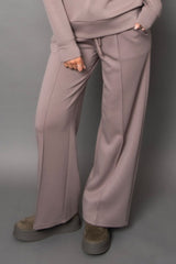 Person wearing light beige/grey pants and a matching top against a gray background