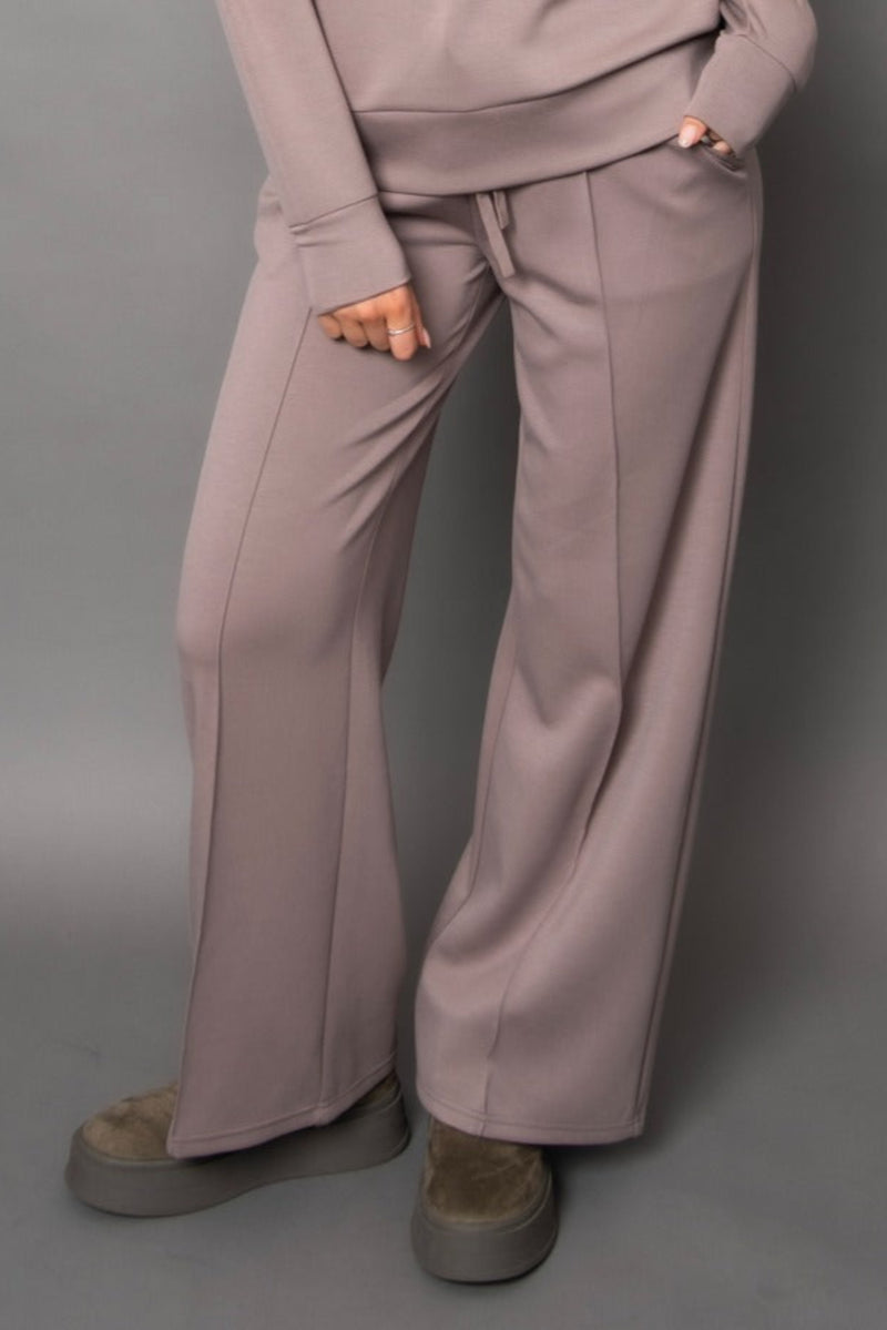 Person wearing light beige/grey pants and a matching top against a gray background