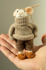 Felted mouse ornament with a beige knitted turtleneck sweater and brown felt pants, held in a hand against a neutral background