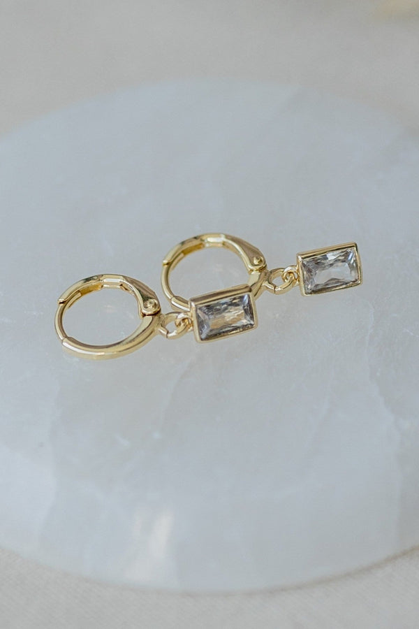 Gold hoop earrings with clear gemstones on a light background