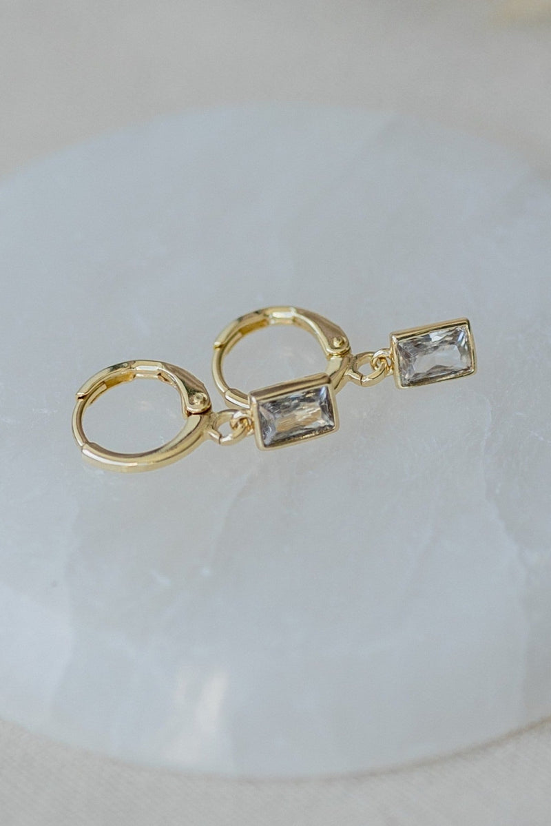 Gold hoop earrings with clear gemstones on a light background