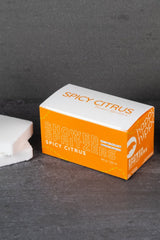 Spicy Citrus Shower Spritzer packaging and sponge on a dark surface.